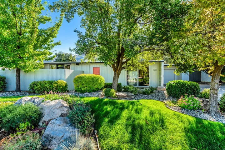 Lush front yard with mature trees, sculpted shrubs, a manicured lawn, and natural rock landscaping