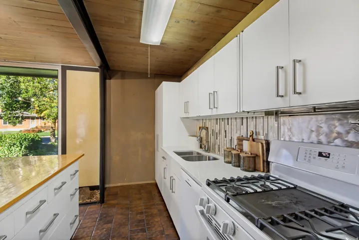White cabinetry with stainless hardware, tiled backsplash, white countertop, double basin sink, and gas range