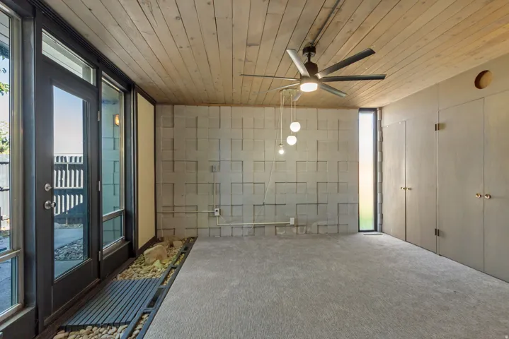 Wood-plank ceiling, textured wall paneling, ceiling fan, full-light entry door, and vertical window