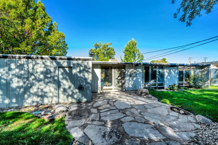 Stone pathway leading to an entry, expansive glass windows, and a level lawn