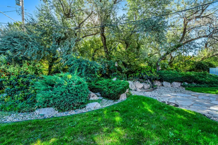 Manicured lawn with mature trees and diverse shrubbery, featuring a flagstone path and rock landscaping