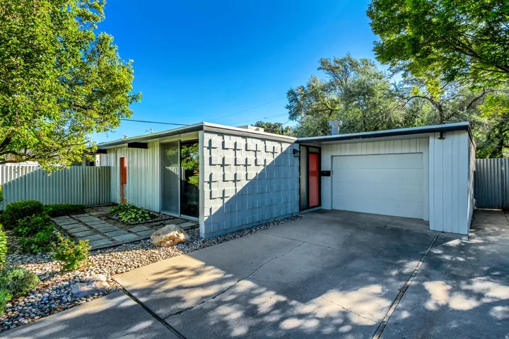 Modern exterior design featuring a flat roofline, attached garage, concrete driveway, and a front entry with a vibrant door