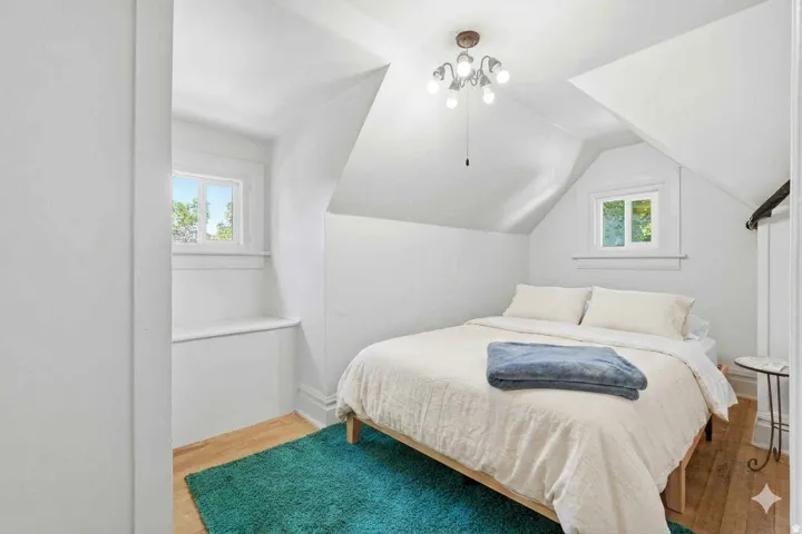 Angled ceiling lines, two casement windows, wood-finish flooring, and a multi-bulb ceiling fixture