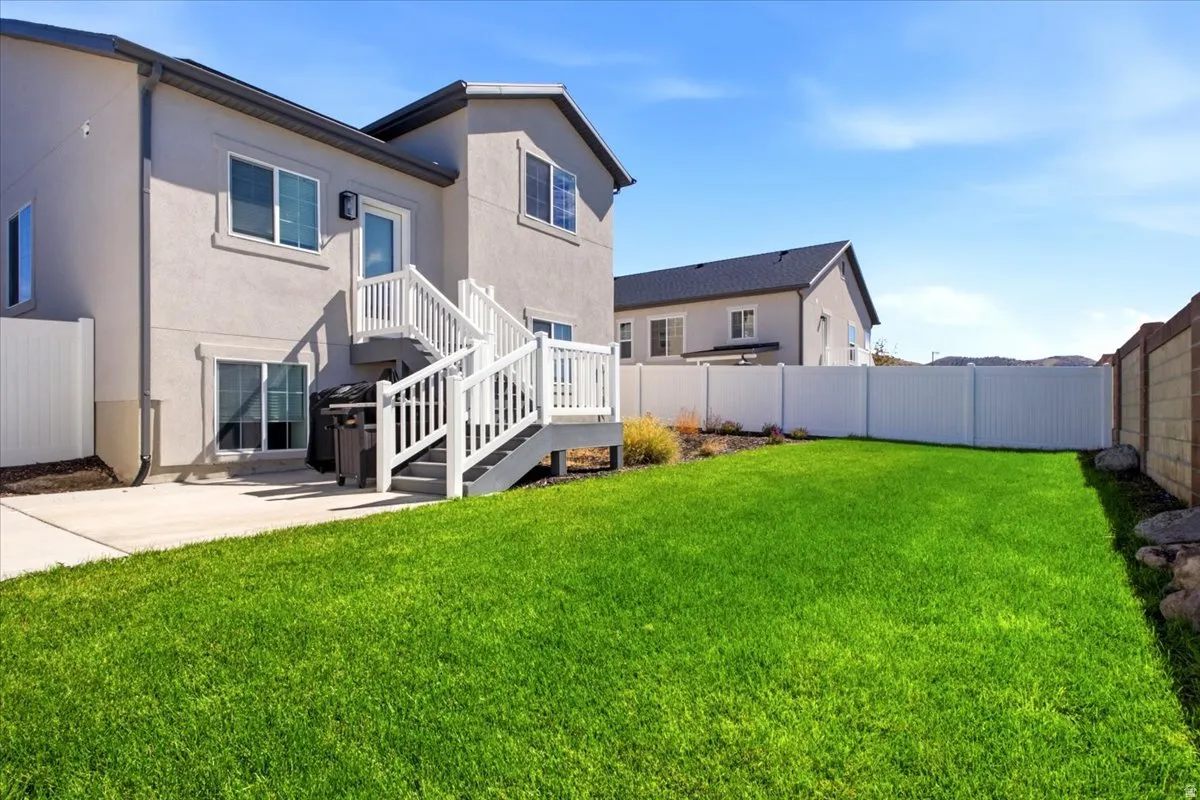 Expansive lawn, concrete patio, white vinyl fencing, and a two-story exterior with an upper-level deck and stairs