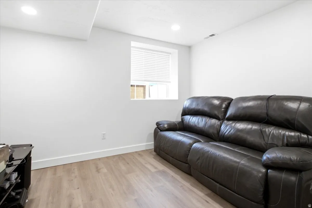 Recessed lighting illuminates the space, featuring a window with horizontal blinds and wood-finish flooring
