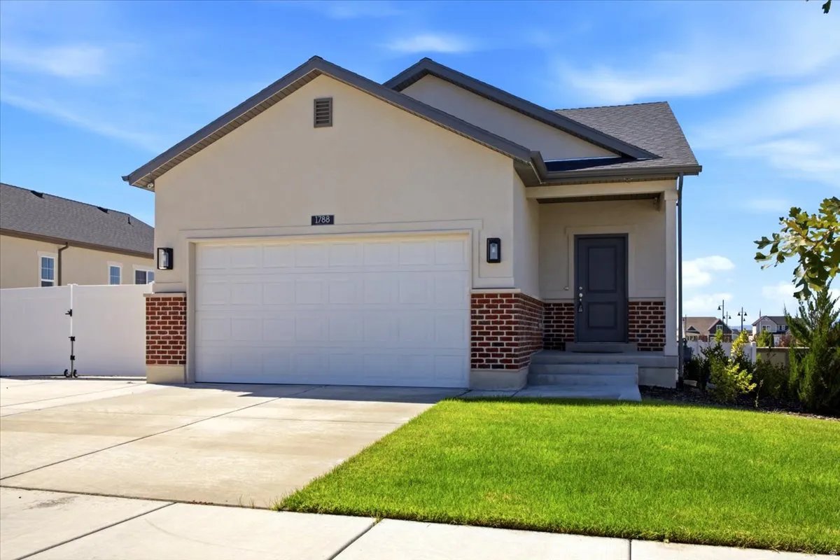 Exterior featuring a covered entry, stucco siding, brick detailing, and an attached two-car garage