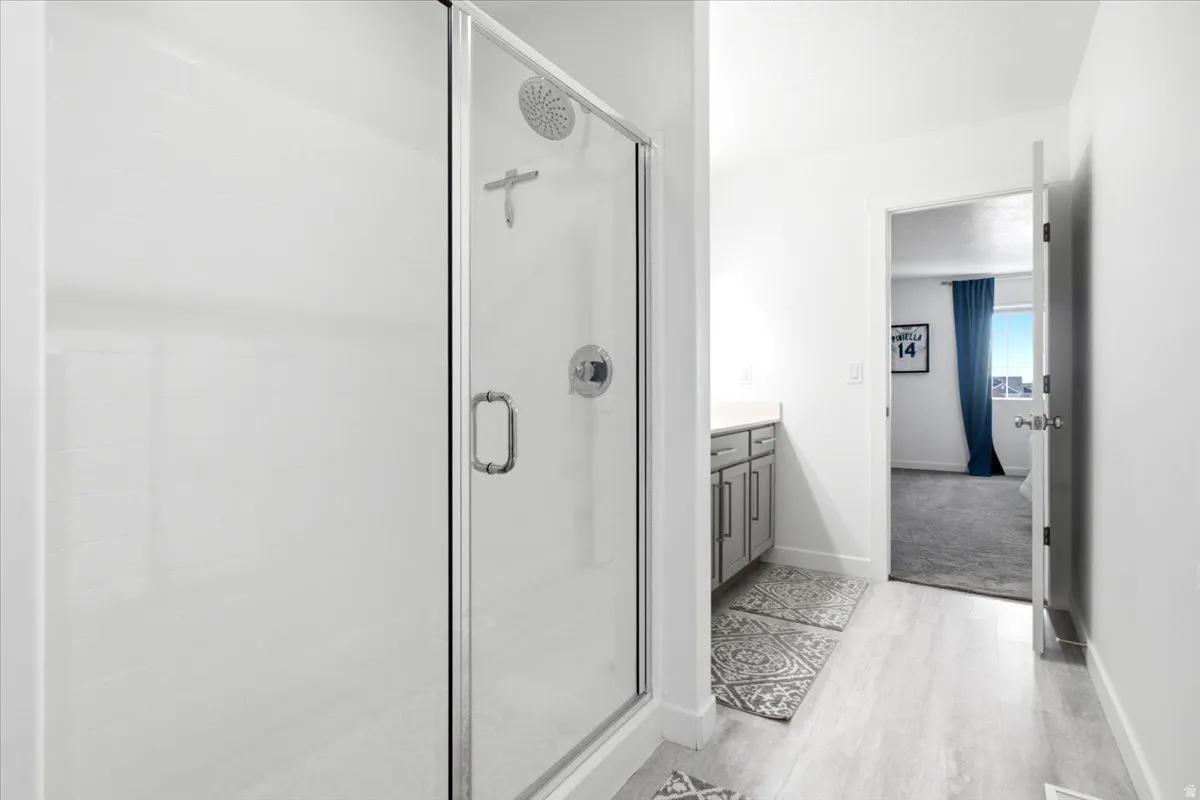 Glass-enclosed shower with a rainfall showerhead, white subway tile surround, wood-finish flooring, and a vanity with a light-colored countertop