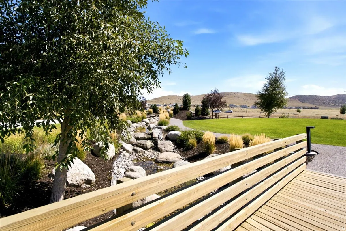 Expansive green space featuring a wooden deck, natural rock landscaping, and mature trees