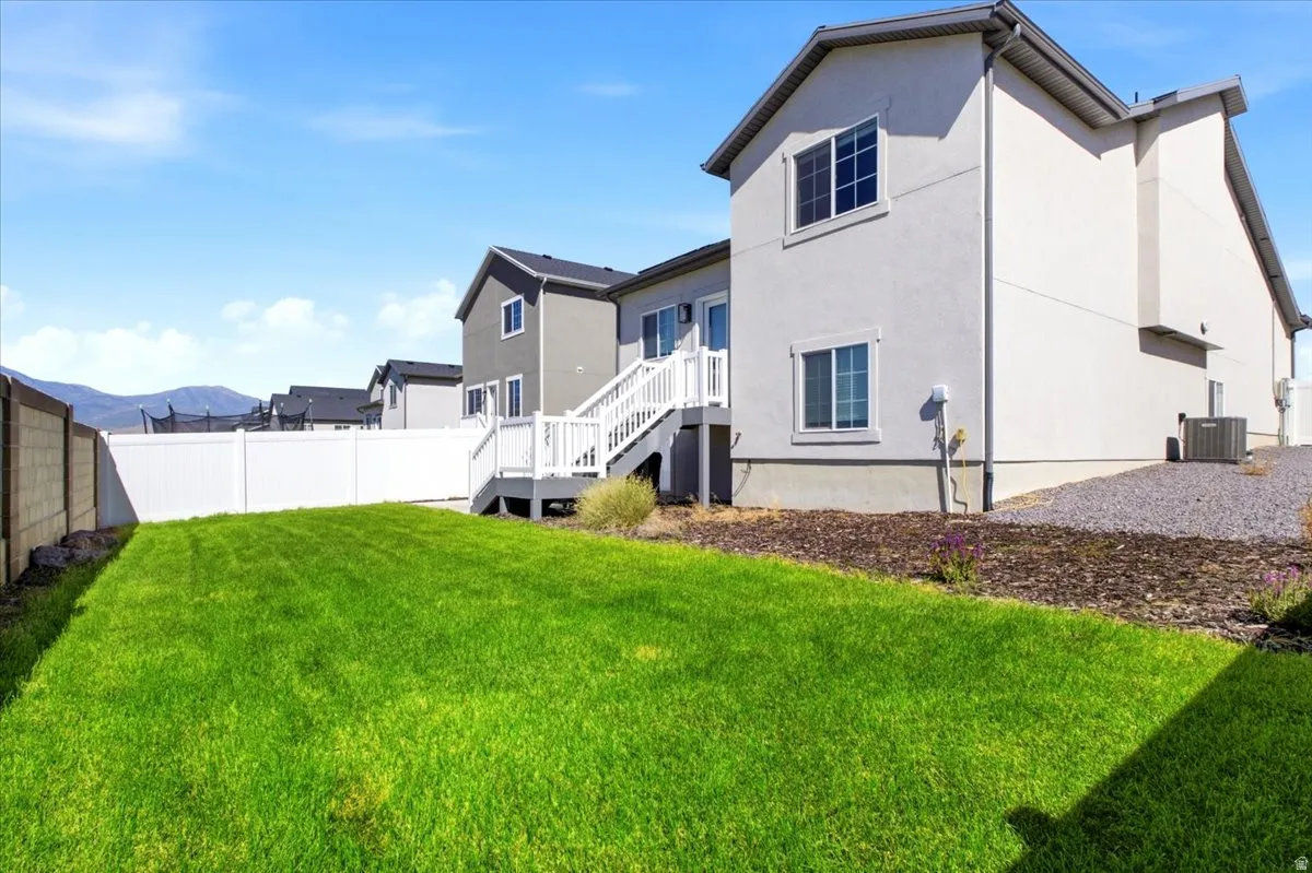 Expansive backyard featuring a green lawn, white vinyl fencing, and a multi-level deck with white railings