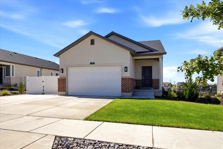 Stucco exterior with brick accents, dark gray pitched roof, integrated two-car garage, and a concrete driveway
