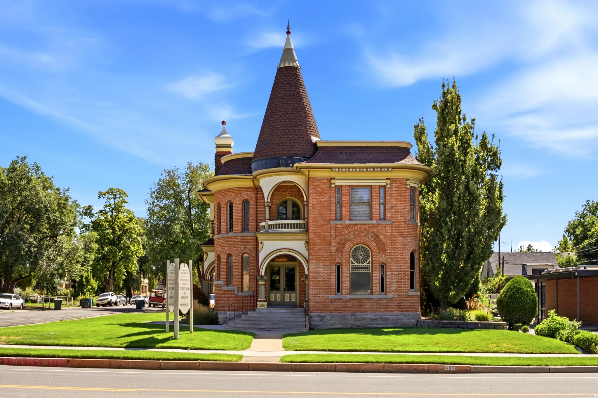 Brick exterior with a conical roof tower, arched entryways, a second-story balcony, and a manicured lawn