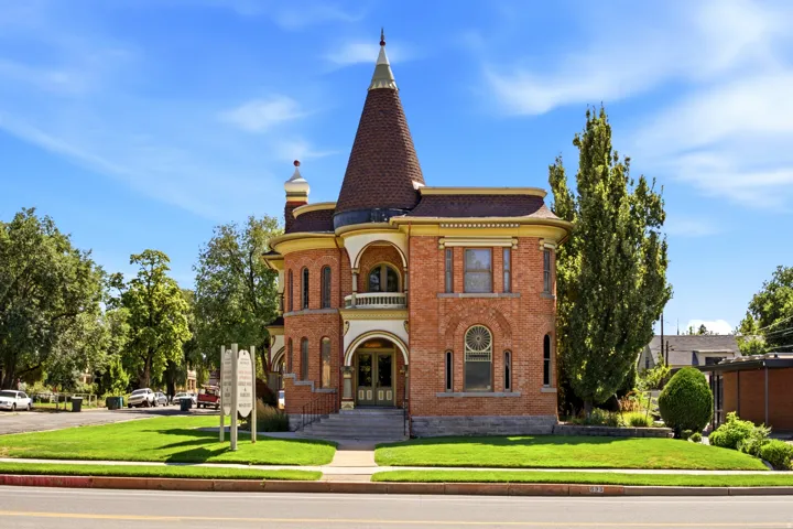 Brick exterior with a conical roof tower, arched entryways, a second-story balcony, and a manicured lawn