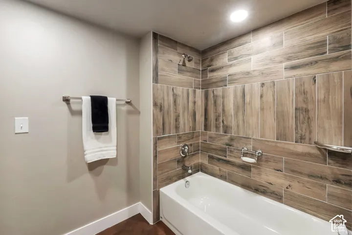 Bathtub with wood-finish tile surround, chrome fixtures, and recessed lighting
