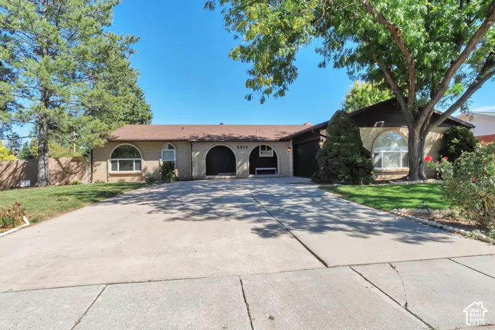 Paved driveway leading to a ranch-style residence featuring arched entryways, arched windows, and mature trees