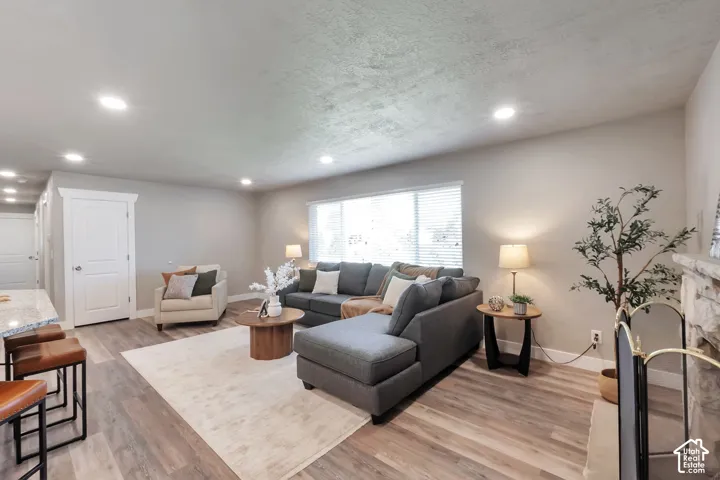 Spacious living area featuring wood-finish flooring, recessed lighting, and a stone-clad fireplace