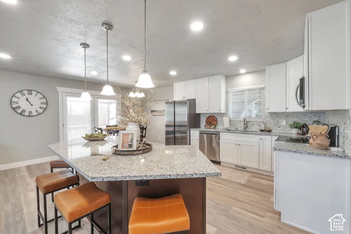 Kitchen featuring a large island with a stone-finish countertop, pendant lighting, white cabinetry, and stainless steel appliances