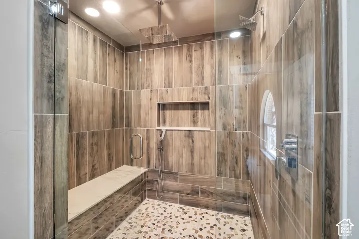 Glass-enclosed shower with wood-look tile surround, built-in bench, recessed niche, and pebble-tile flooring