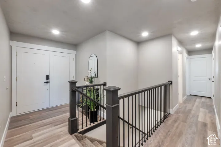 Double entry doors with contemporary hardware, wood-finish flooring, recessed lighting, and a dark wood and metal stair railing