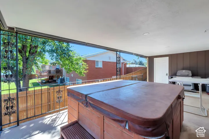 Covered outdoor patio with a built-in spa, dark wrought iron railings, and a wood privacy fence
