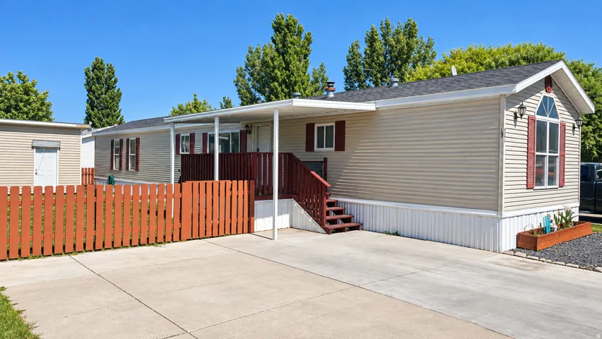Beige siding exterior with a covered porch, red-stained wooden fence, and paved driveway