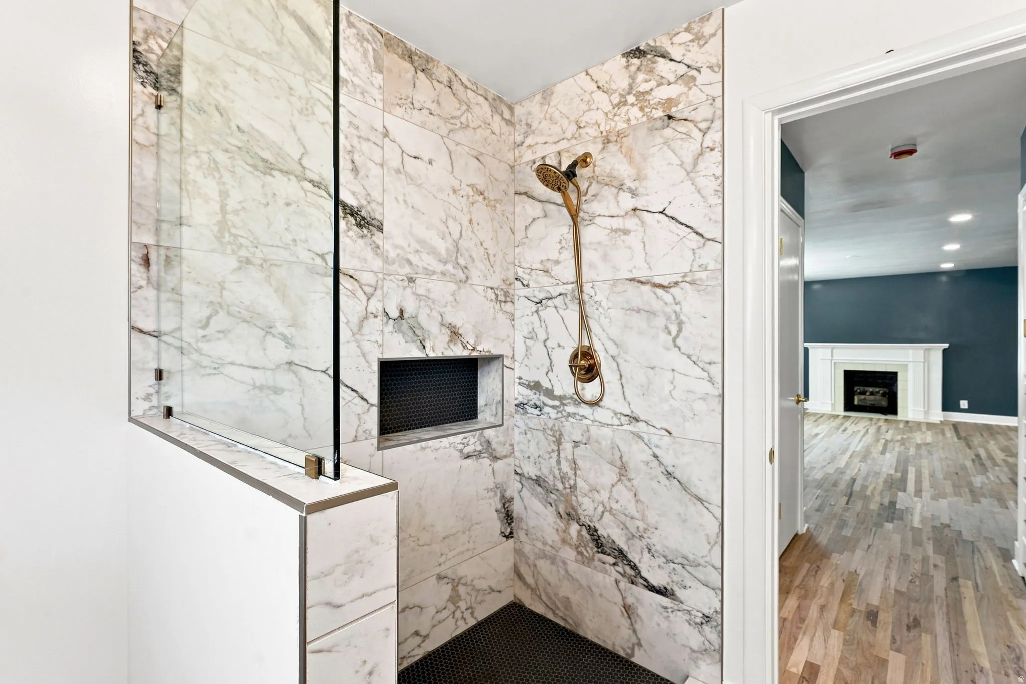 Walk-in shower with full-height marble-patterned tile, glass partition, recessed shower niche, and a bronze-finish shower system