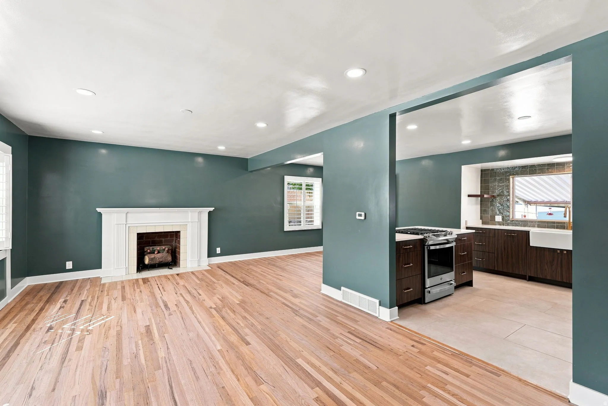Hardwood-style flooring throughout, white fireplace with decorative mantel, recessed ceiling lighting, kitchen features a stainless steel range, and a white farmhouse sink