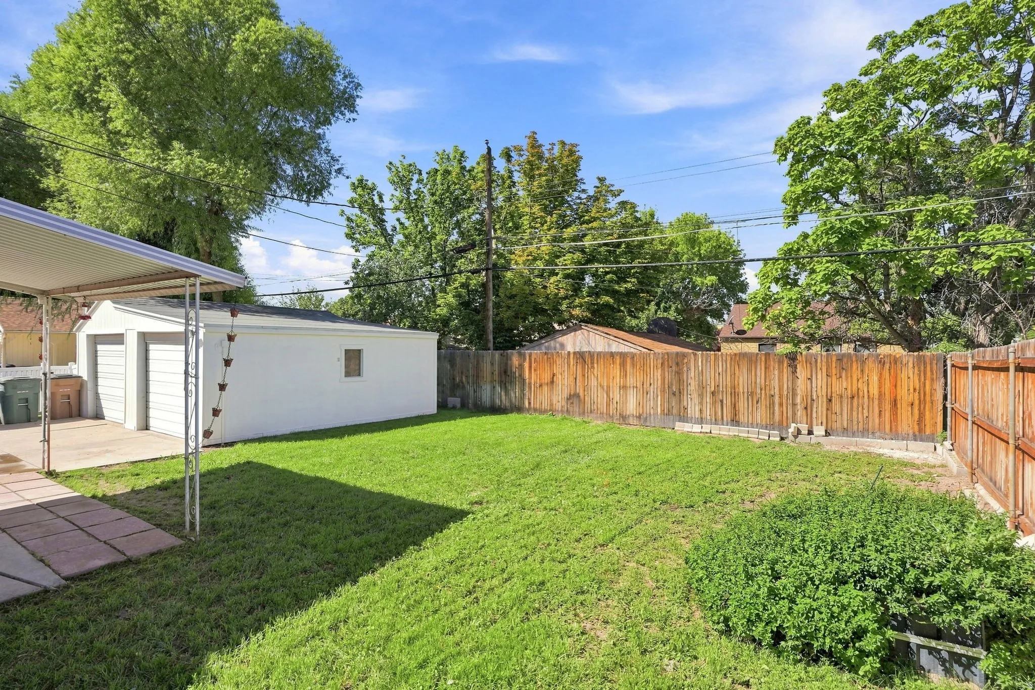 Expansive green space featuring a detached two-car garage, partial patio, partial wood fencing, and mature perimeter trees