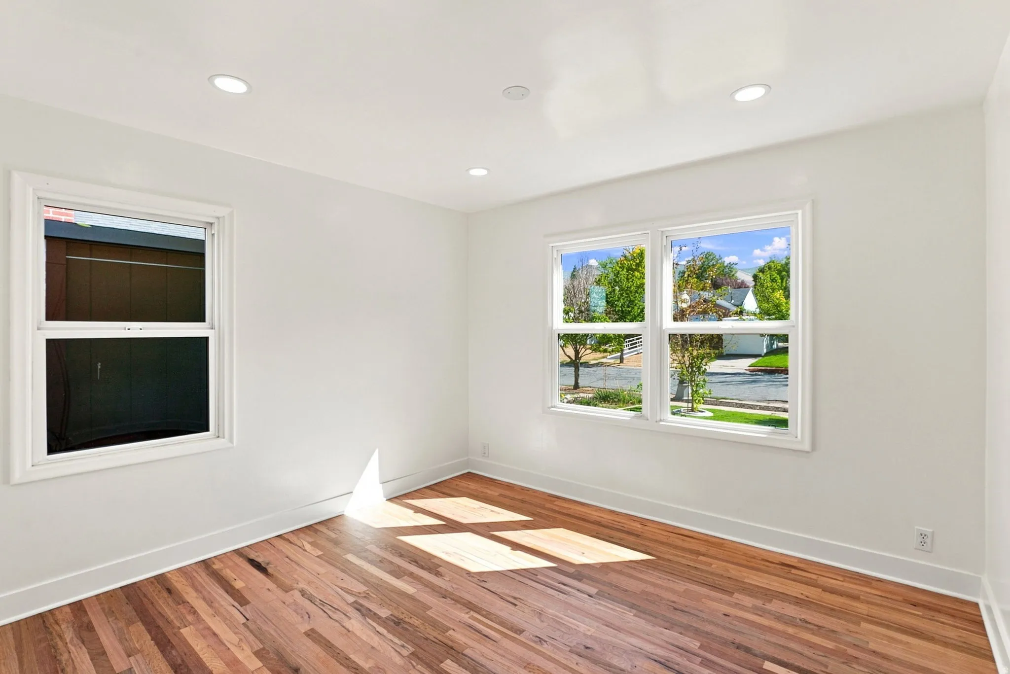 Recessed lighting, warm wood flooring, crisp white walls, and multiple windows
