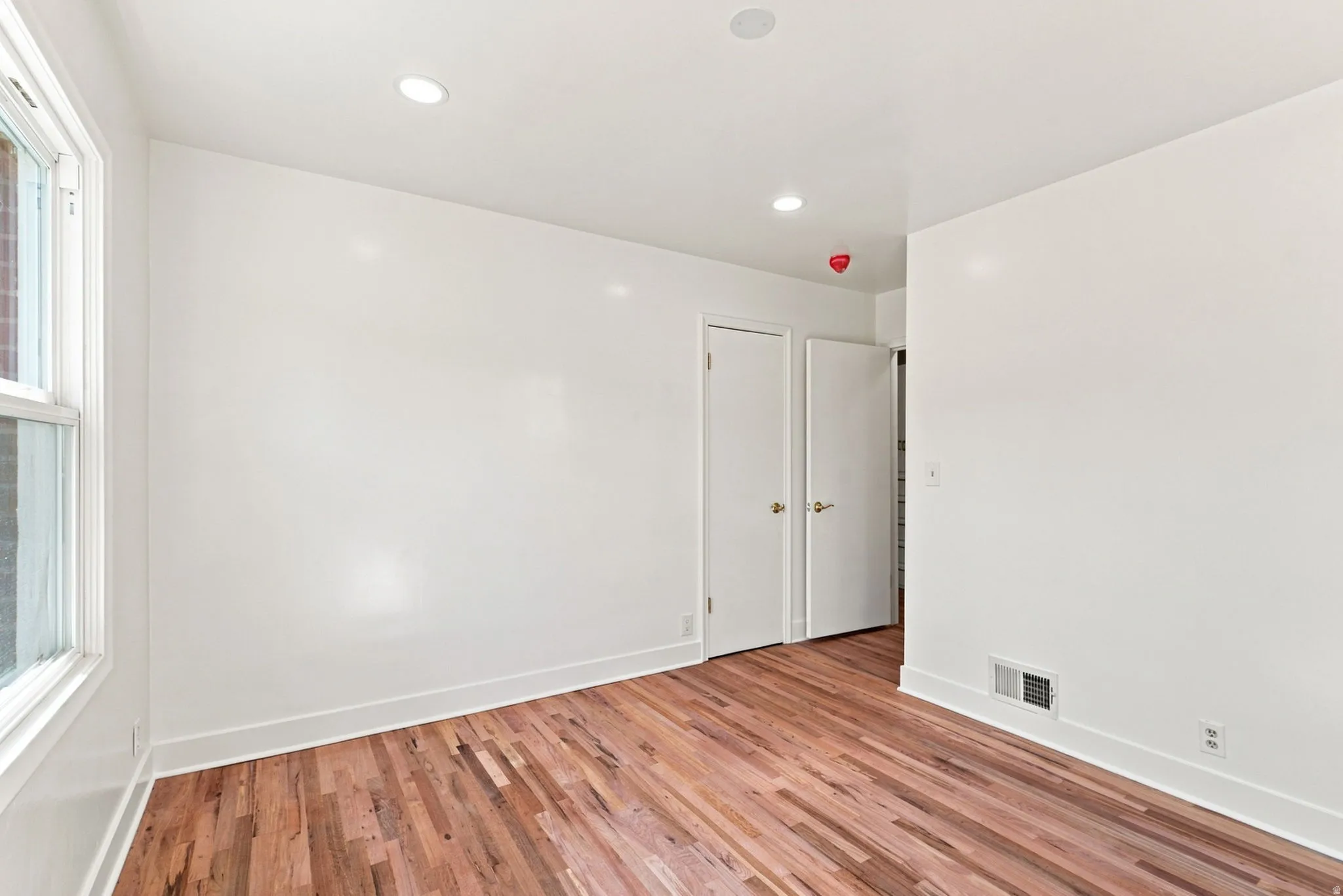 Hardwood flooring, recessed lighting, white walls, and a window with white trim