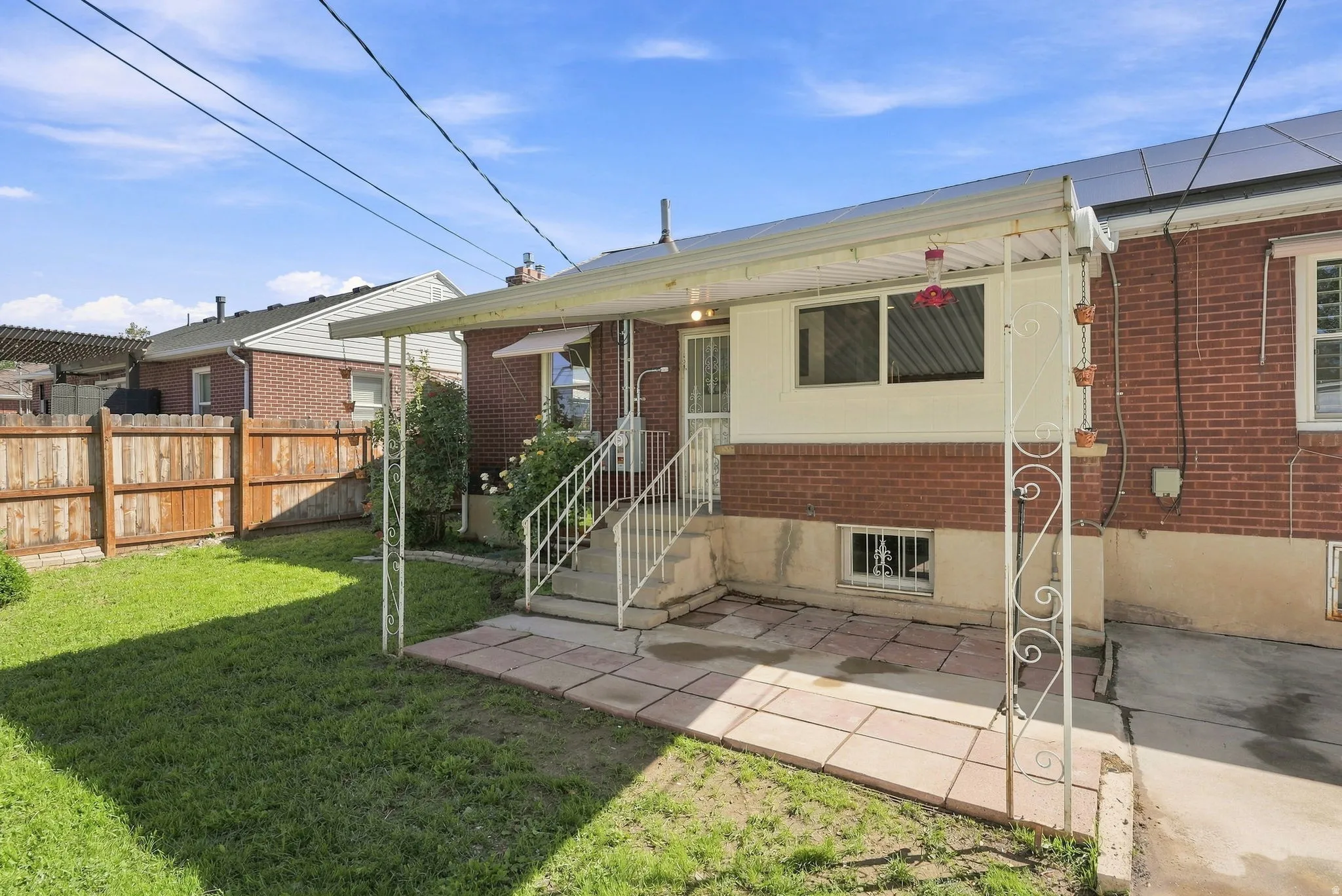 Brick exterior with white trim, covered patio, fenced yard, and exterior stairs with white railings
