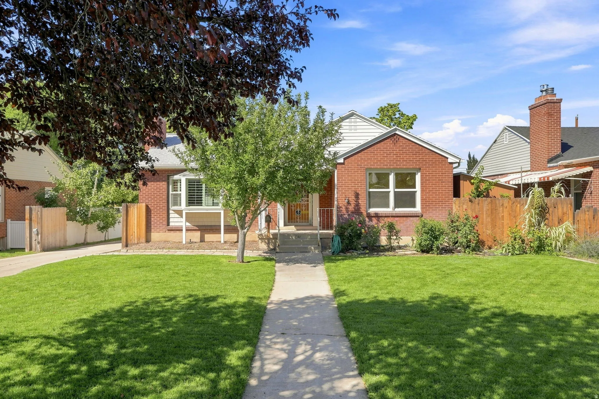 Brick exterior with white trim, front porch with railings, mature trees, manicured lawn, and paved walkway