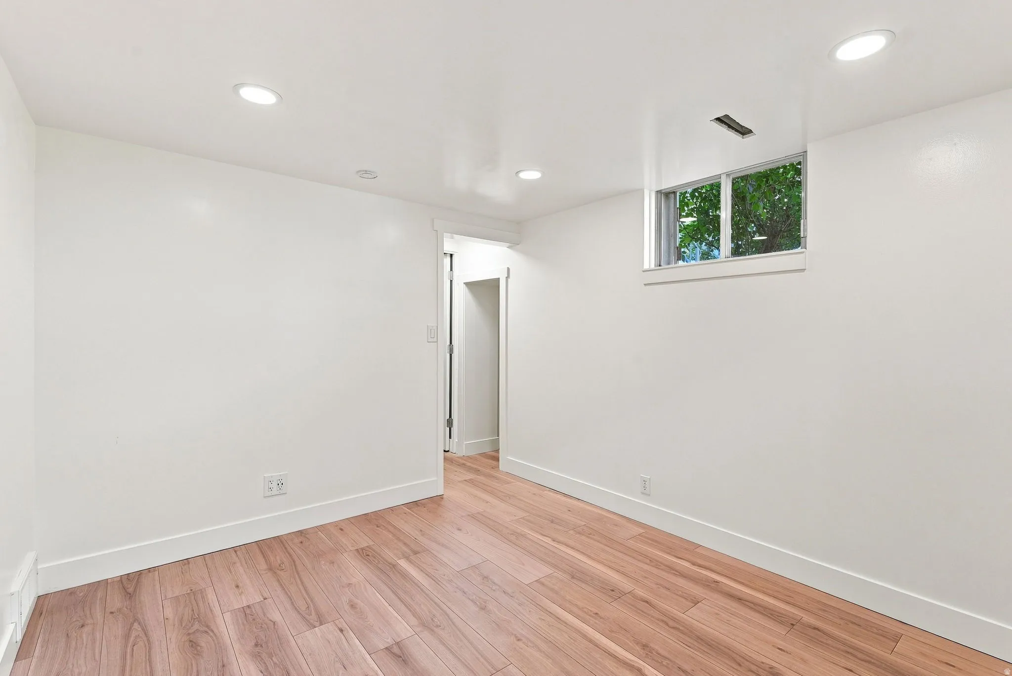 Recessed ceiling lighting, wood-finish flooring, white walls, and a window with trim