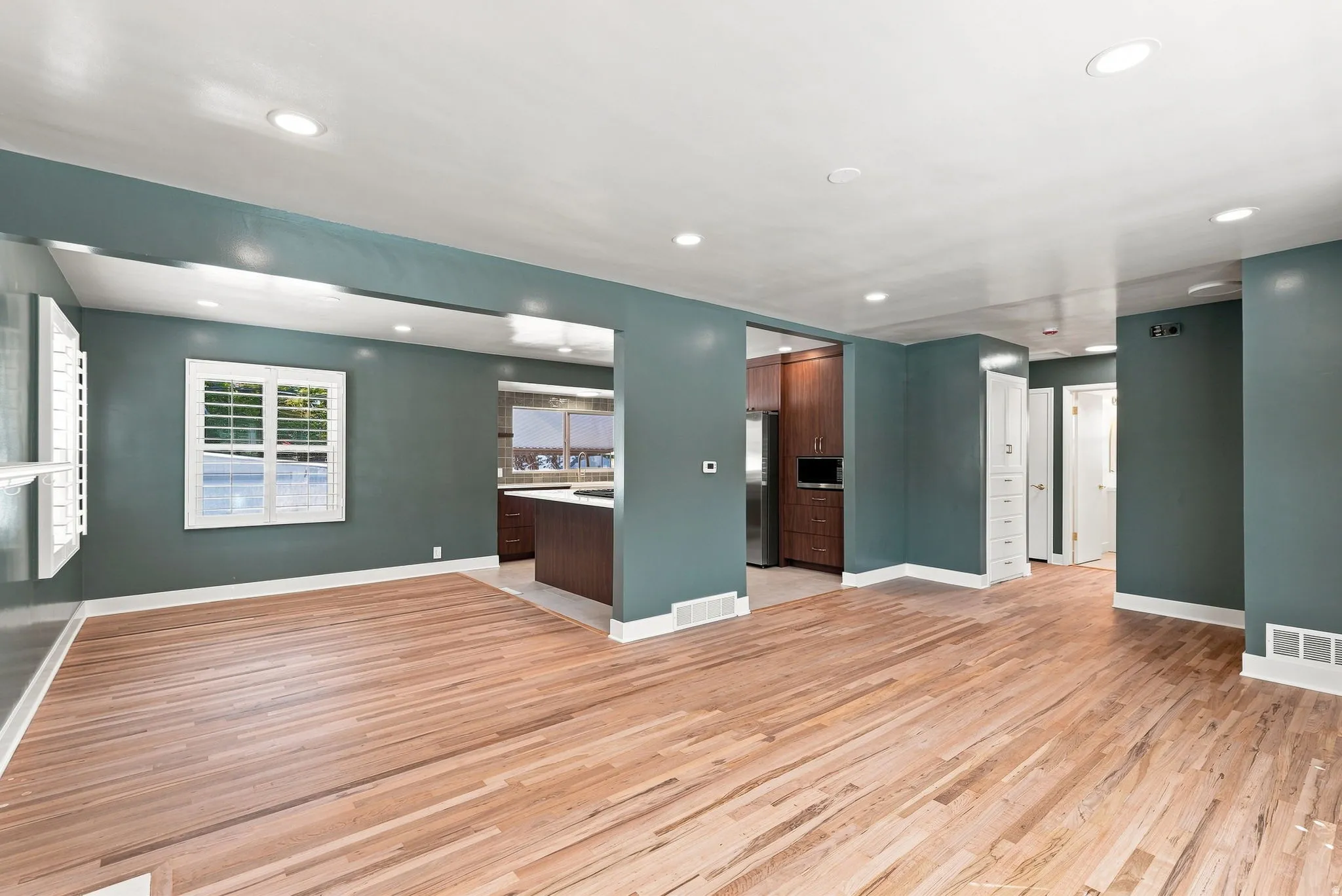 Hardwood flooring throughout, recessed ceiling lighting, window with white plantation shutters, built-in cabinetry, and a kitchen with dark wood-finish cabinetry