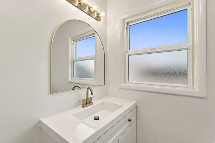 White vanity with integrated sink and brushed brass faucet, framed by an arched mirror and a three-light vanity fixture