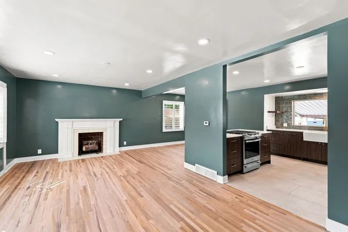 Hardwood-style flooring throughout, white fireplace with decorative mantel, recessed ceiling lighting, kitchen features a stainless steel range, and a white farmhouse sink