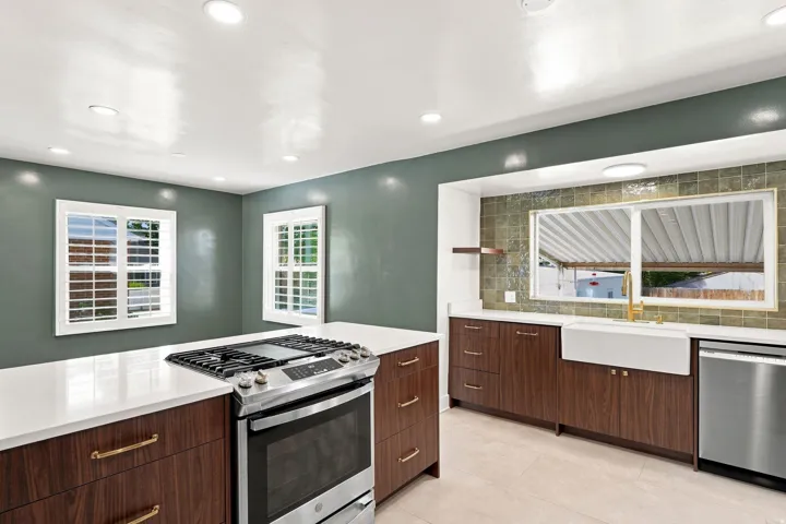 Modern kitchen featuring wood-finish cabinetry, white countertops, stainless steel appliances, and a farmhouse sink