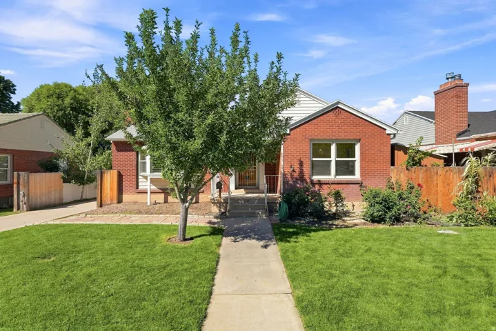 Brick exterior with white trim, a concrete pathway, a mature tree, and a wooden fence