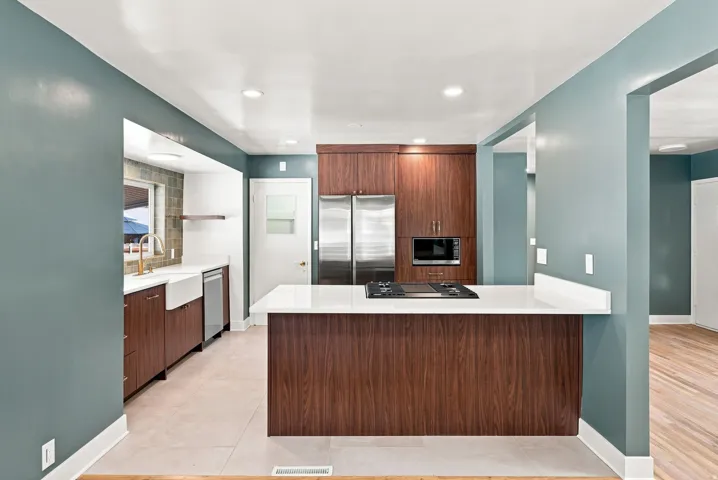 Kitchen featuring wood-finish cabinetry, stainless steel appliances, a white farmhouse sink, a gas cooktop, and a white countertop