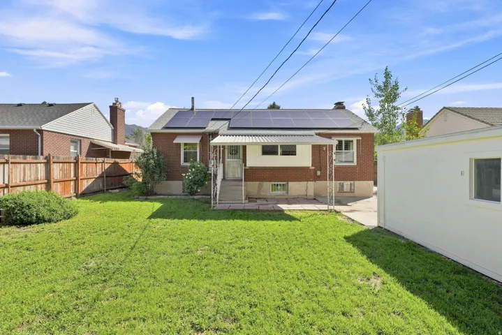 Brick exterior, solar panel array, attached awning, concrete patio, and fenced yard