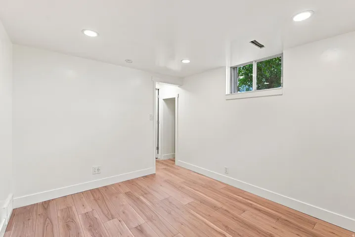 Recessed ceiling lighting, wood-finish flooring, white walls, and a window with trim
