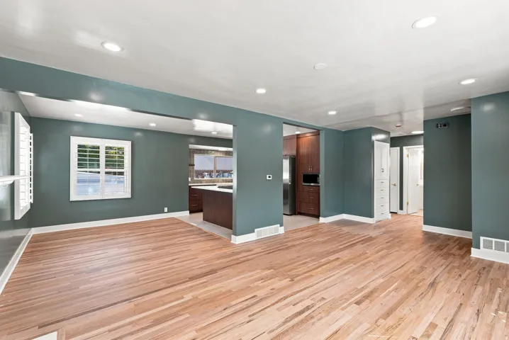 Hardwood flooring throughout, recessed ceiling lighting, window with white plantation shutters, built-in cabinetry, and a kitchen with dark wood-finish cabinetry