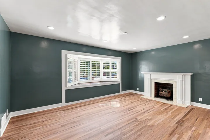 Hardwood flooring, recessed lighting, bay window with plantation shutters, decorative fireplace with mantel, and white trim