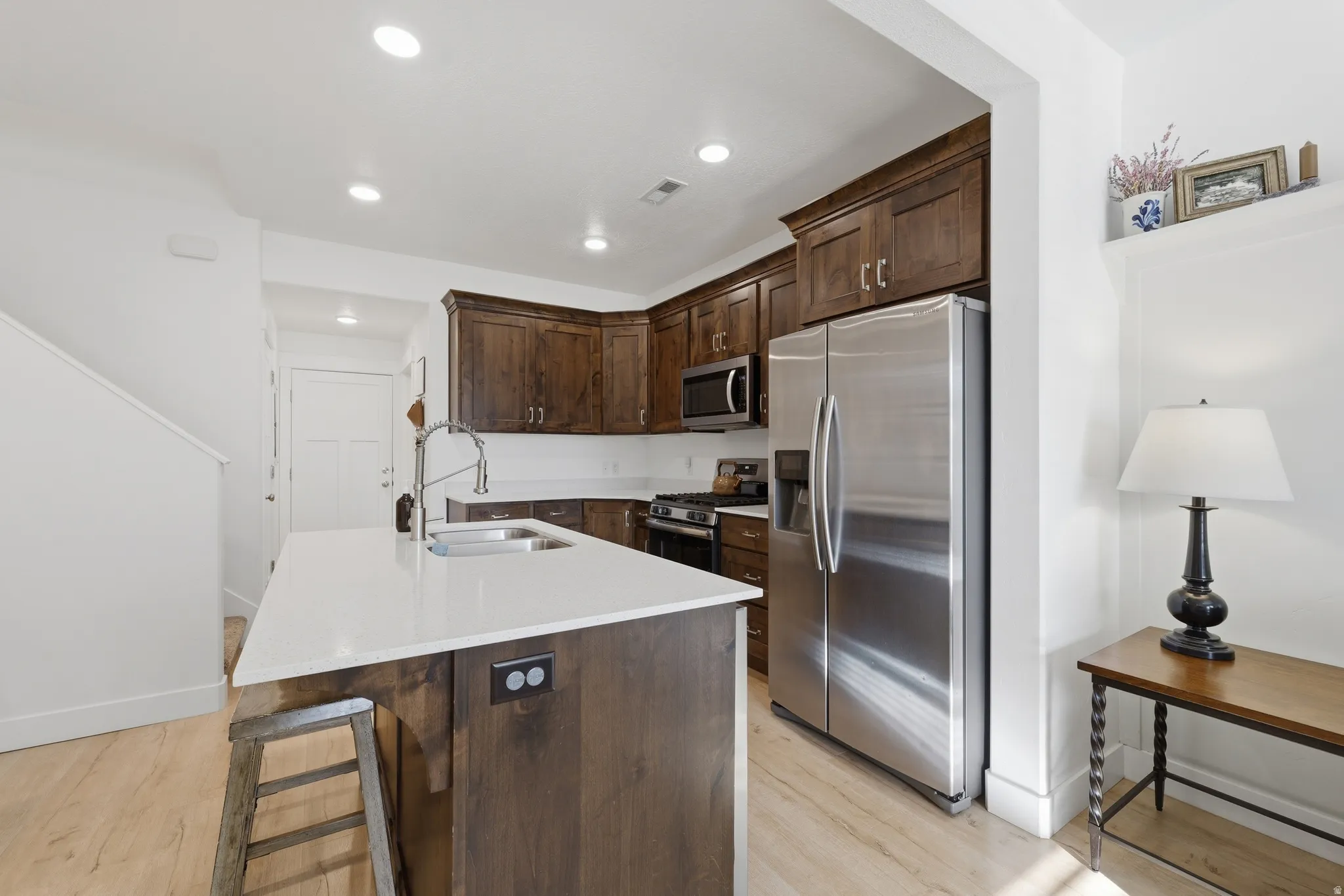Kitchen featuring a central island with white countertop, dark wood-finish cabinetry, stainless steel appliances, and wood-finish flooring