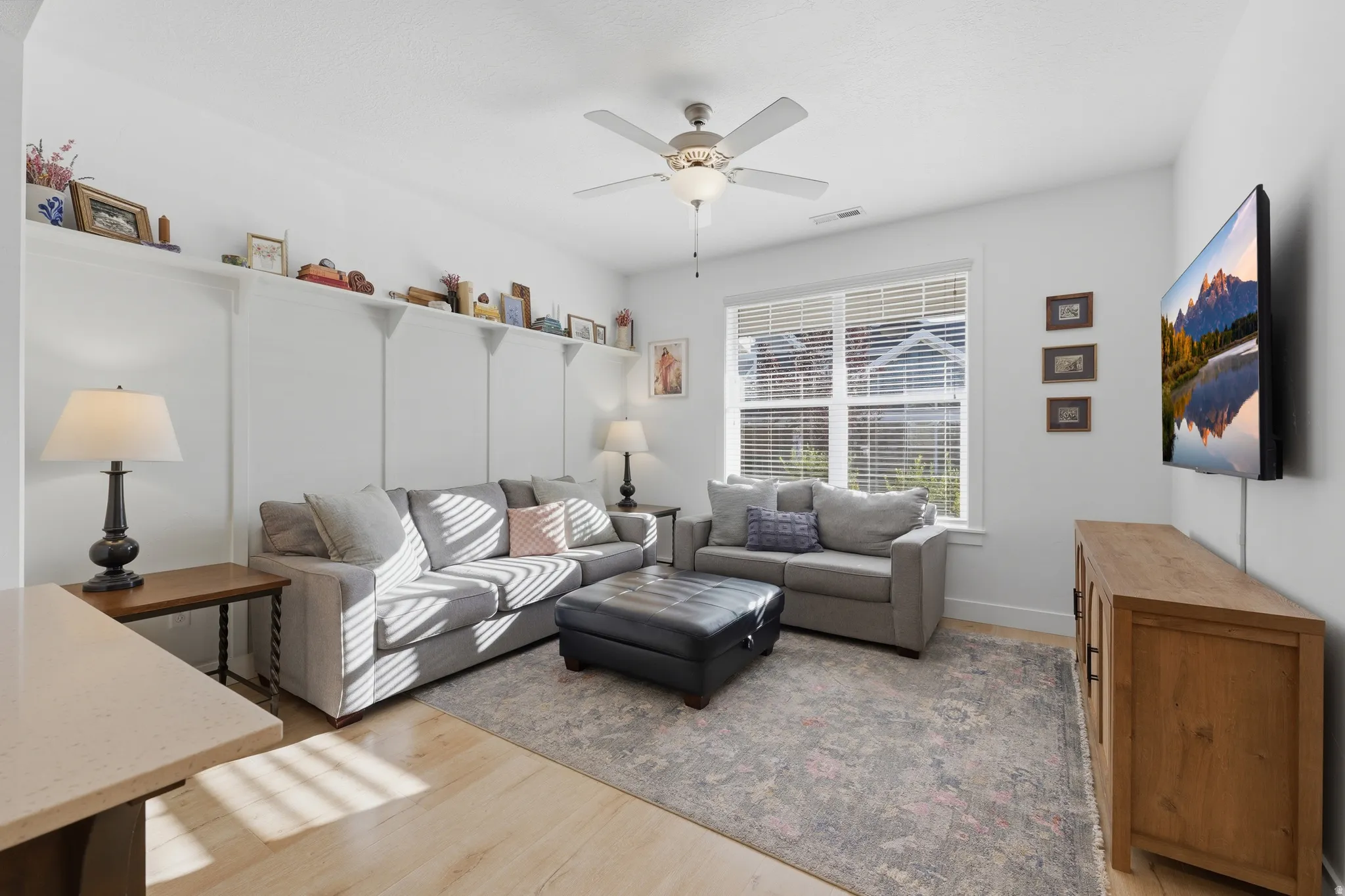 Light wood-finish flooring, built-in shelving, ceiling fan with integrated lighting, window with blinds, and white trim