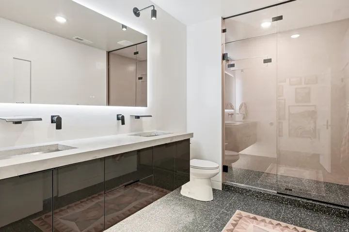 Dual vanity with integrated concrete sinks, wall-mounted matte black faucets, and a backlit mirror