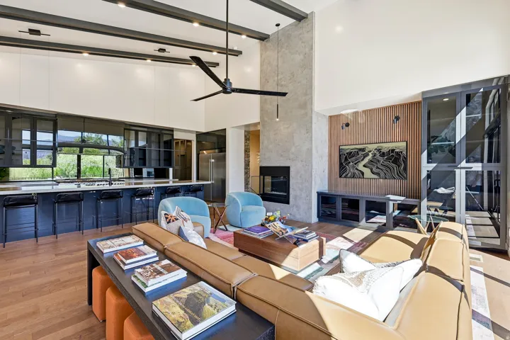 Open-concept living space with vaulted ceilings, exposed beams, a built-in fireplace, a large kitchen island with integrated seating, and wood-finish flooring