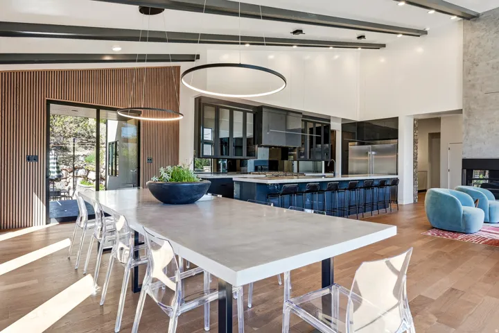 Vaulted ceiling with exposed beams, wood-finish flooring, full-height stone fireplace, wood-slat accent wall, and a large sliding glass door