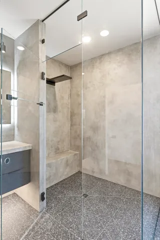 Walk-in shower with terrazzo flooring, concrete walls, a built-in bench, and glass enclosure