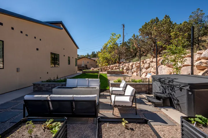 Expansive outdoor space featuring a hot tub, fire pit, stone retaining wall, raised garden beds, and manicured lawn