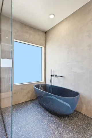 Freestanding soaking tub with a wall-mounted faucet, terrazzo tile flooring, and a glass-enclosed shower
